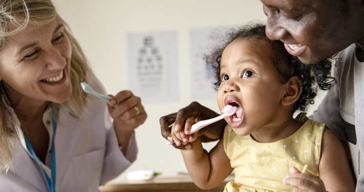 parent and doctor showing child how to brush teeth